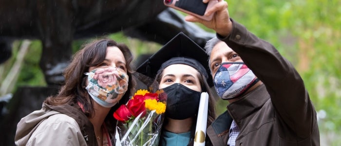 mom and dad with graduating daughter taking a selfie with bouquet outside