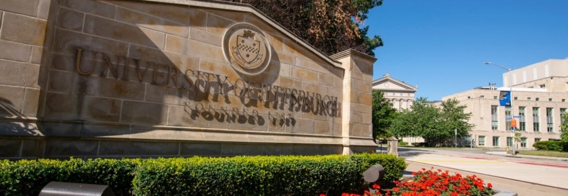 university of pittsburgh stone sign with red flower bed at base